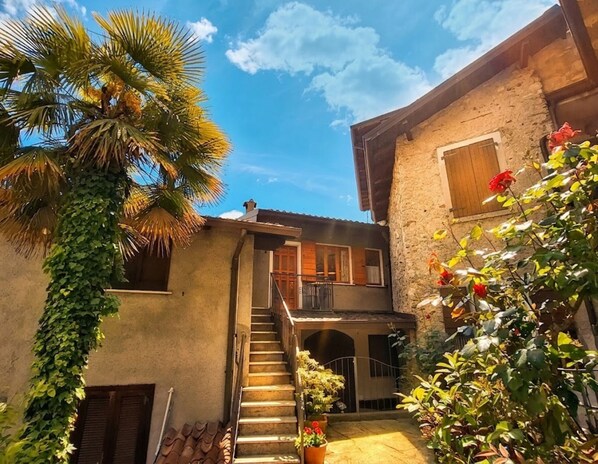 A courtyard with a staircase leading to a second floor, surrounded by buildings with stone walls and wooden shutters. - Sompriezzo: Lake View (Tremosine)