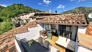 A residential building with a tiled roof, a balcony with a table and chairs, and a view of the surrounding hills. - Sompriezzo: Lake View (Tremosine)