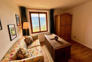A room with a sofa, a wooden table, a window with a view of mountains, and a wardrobe. - Sompriezzo: Lake View (Tremosine)