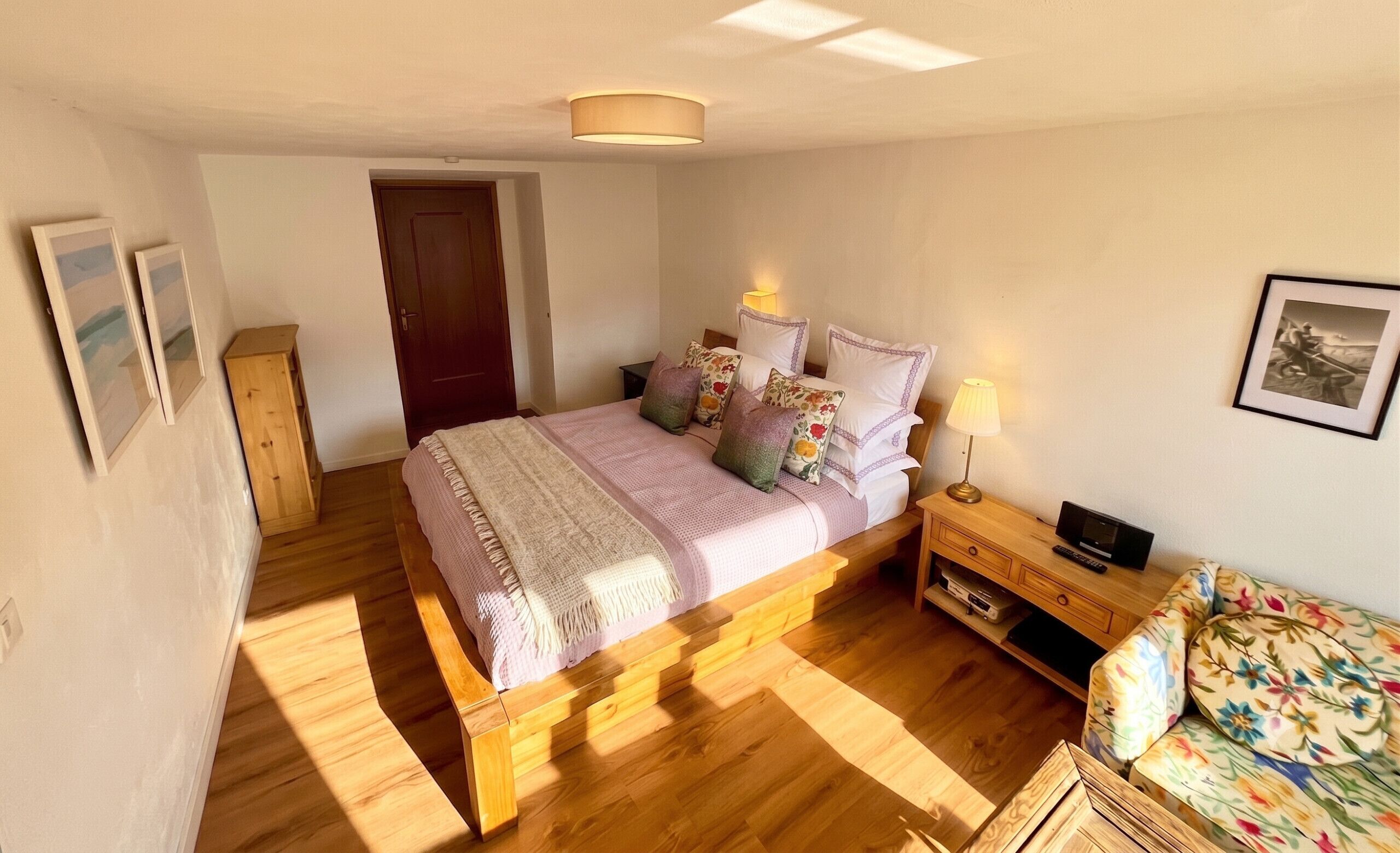 Una camera da letto con un letto di legno, un comodino con una lampada, un tavolino con un telecomando e un quadro appeso al muro.