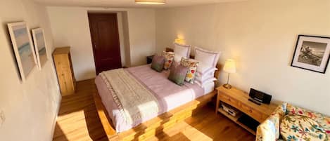Un dormitorio con una cama de madera, una mesita de noche con una lámpara, una pequeña mesa con un control remoto y un cuadro colgado en la pared.