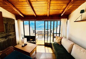 A room with a wooden ceiling, a sofa, a table, and a view through large windows to the outdoors. - Sompriezzo: Lake View (Tremosine)