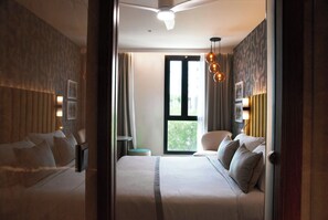 A hotel room with a bed, a chair, a small table, and a window with a view. - Leonardo Royal Hotel Madrid Valdebebas (Madrid)