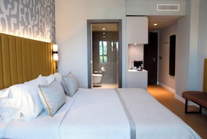 A hotel room with a large bed, a bedside table, a mirror, and a bathroom visible through an open door. - Leonardo Royal Hotel Madrid Valdebebas (Madrid)