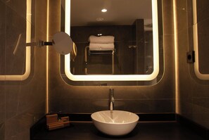 A bathroom with a round mirror, a white sink, and a towel rack. - Leonardo Royal Hotel Madrid Valdebebas (Madrid)