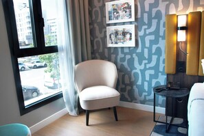 A room with a large window, a chair, a small table with a phone, and a wall with abstract patterns. - Leonardo Royal Hotel Madrid Valdebebas (Madrid)