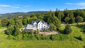 A large, modern house surrounded by lush greenery and trees, with a hilly landscape in the background. - **Private Mountain Retreat with Exceptional Panoramic Views for 4 persons** (Winterberg)