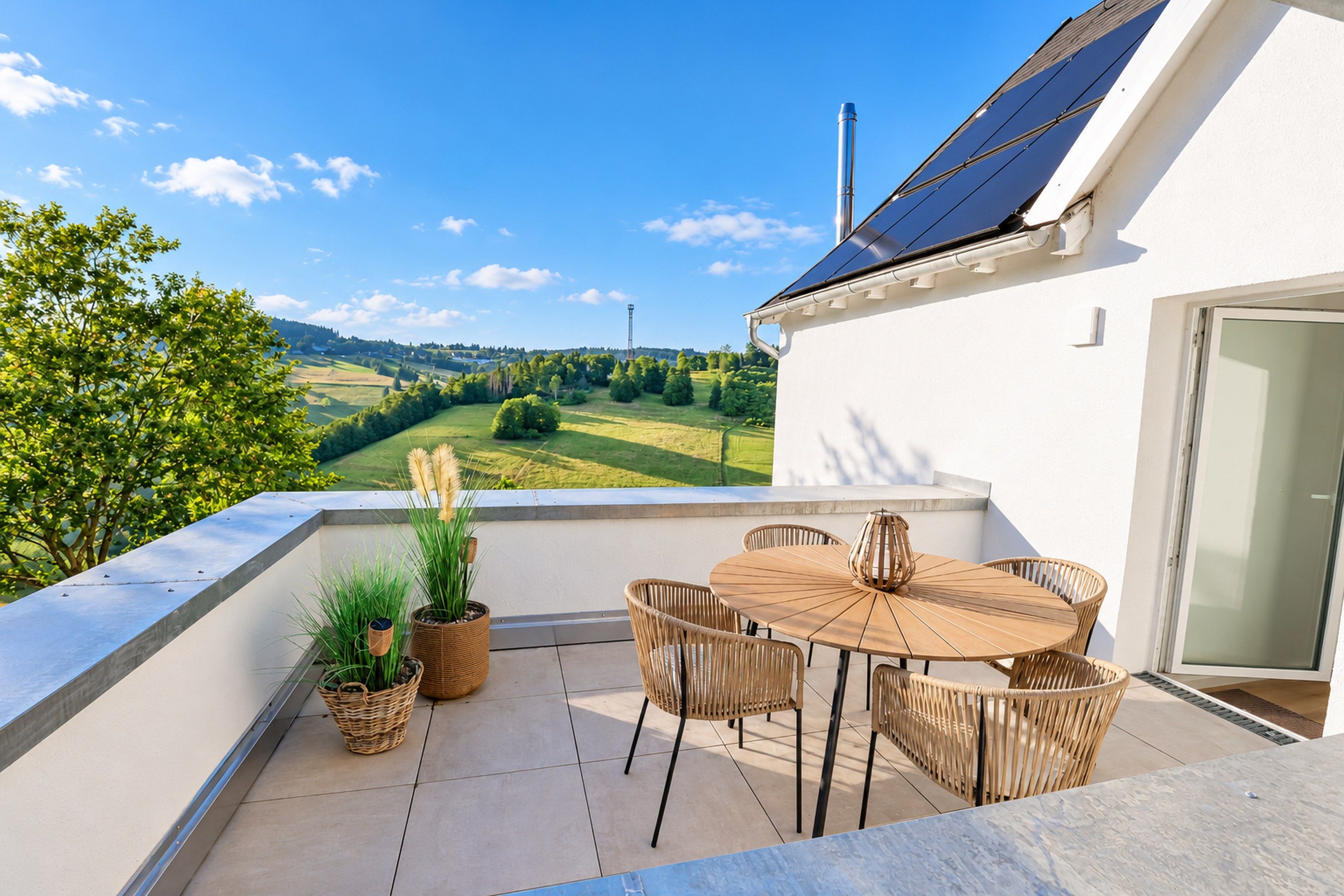 A terrace with a table and chairs, a view of a green landscape, and a building with solar panels.