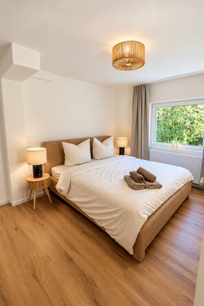 A bedroom with a large bed, two bedside tables with lamps, a window with curtains, and a view of greenery outside. - **Private Mountain Retreat with Exceptional Panoramic Views for 4 persons** (Winterberg)