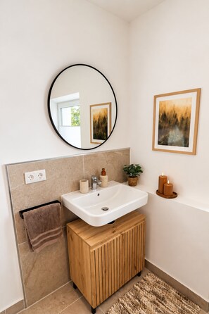 Un baño con un lavamanos blanco, un mueble de tocador de madera, un espejo y dos cuadros en la pared.