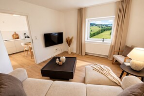 A modern living room with a flat-screen TV, a coffee table with decorative items, a sofa, and a view of a green landscape through a large window. - **Private Mountain Retreat with Exceptional Panoramic Views for 4 persons** (Winterberg)