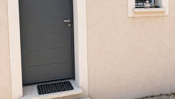 A modern building with a dark grey door, a small window with a metal grille, and a wall-mounted light fixture.