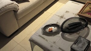 Un salon avec un canapé beige, des coussins à motifs, une petite table avec un plateau et une télécommande.