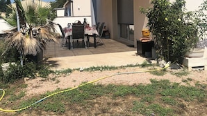 Een overdekt terras met een tafel, stoelen, een palmboom en een tuinslang.