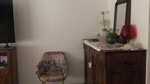 Une pièce avec un meuble en bois, un téléviseur posé sur un meuble, une chaise à motifs et un miroir accroché au mur.