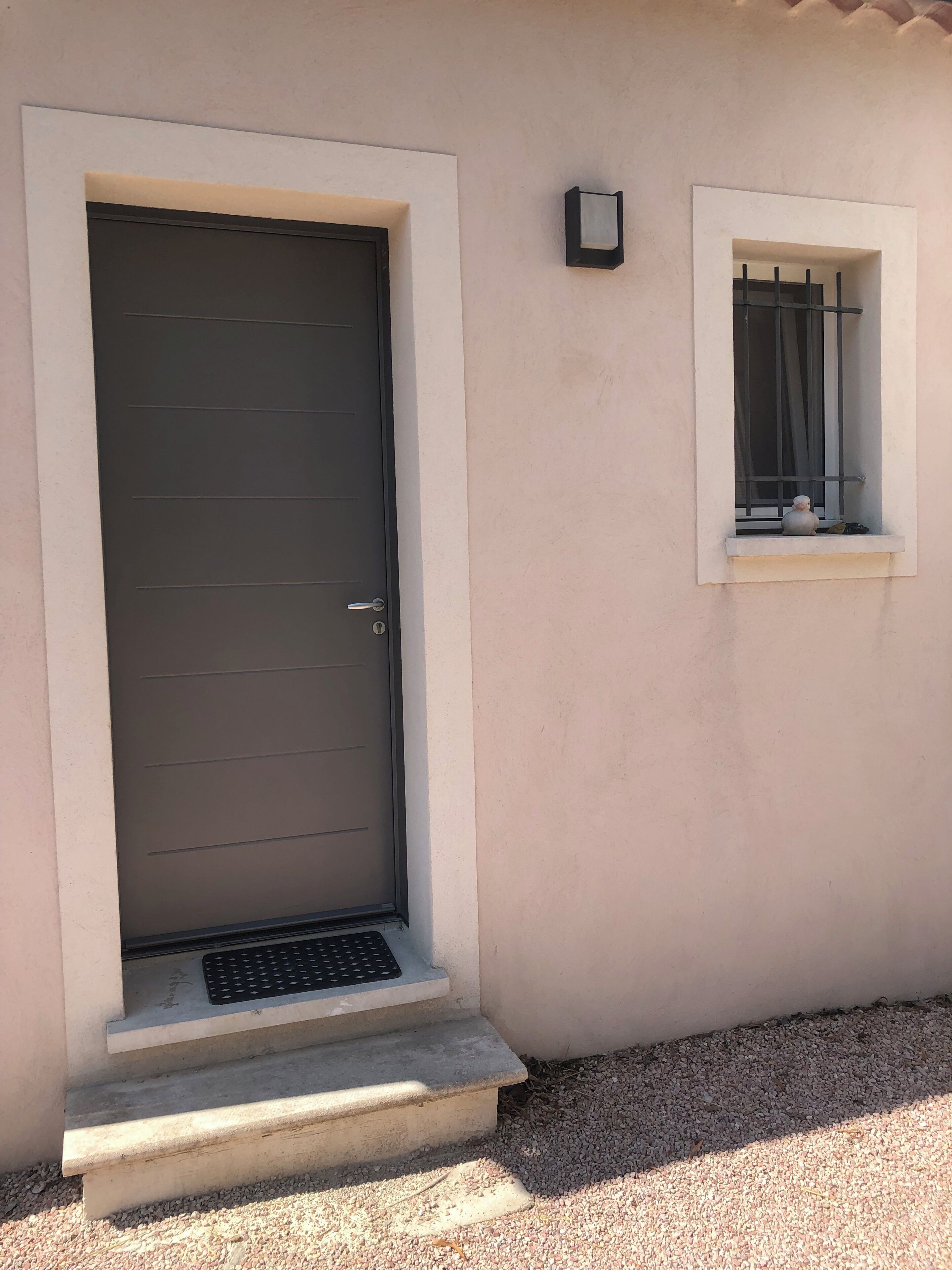 Une porte dotée d’une poignée en métal, une petite fenêtre avec une grille en métal et une marche en béton menant à la porte.