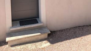 Une porte dotée d’une poignée en métal, une petite fenêtre avec une grille en métal et une marche en béton menant à la porte.
