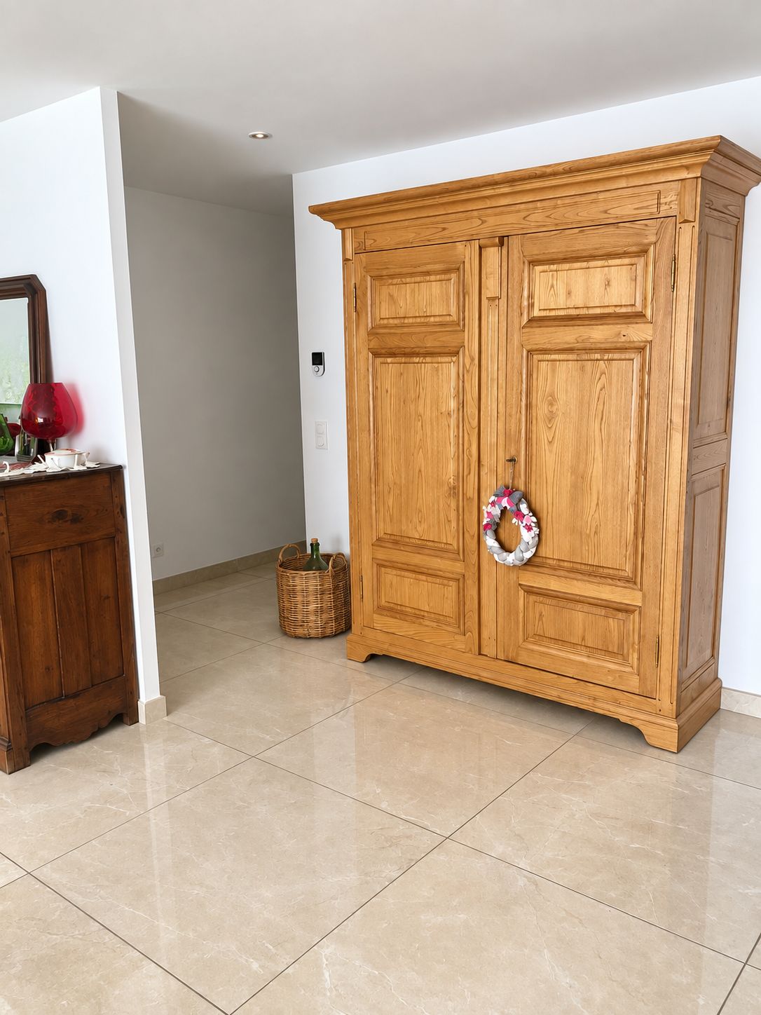 A wooden wardrobe with a mirror and a red object on a dresser.