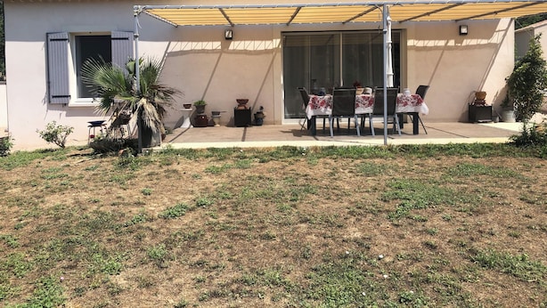 Een huis met een patio, compleet met een tafel en stoelen, omringd door potplanten en een overdekte zithoek.