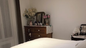 Een slaapkamer met een bed, een kaptafel met decoratieve objecten en een nachtkastje met een lamp.