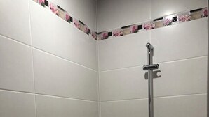 Een hoek van een badkamer met witte betegelde wanden en een douchegedeelte met een handdouche.