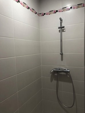 Un angolo di un bagno con pareti piastrellate di bianco e uno spazio doccia con soffione manuale.