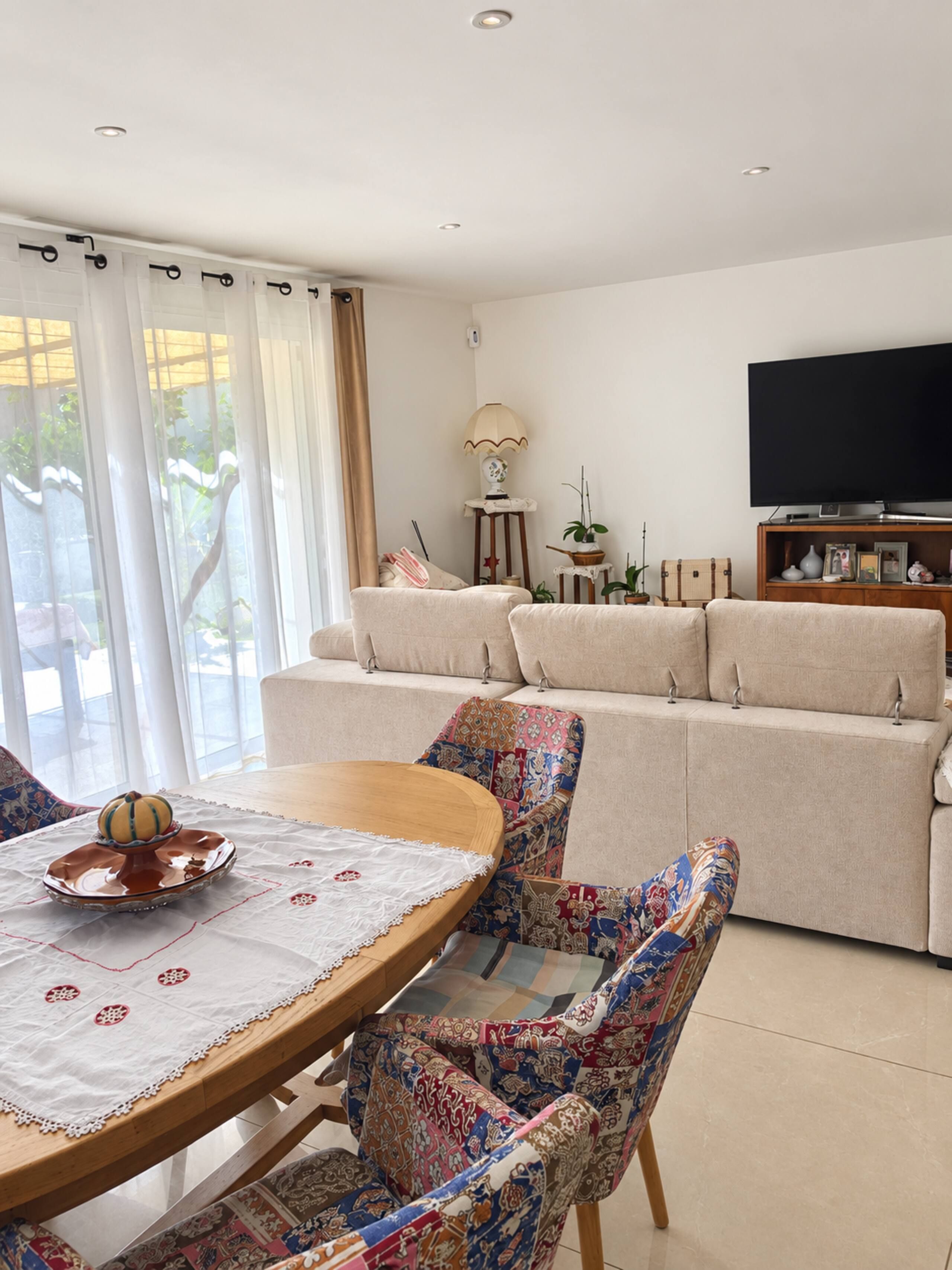 Een woonkamer met een bank, een televisie en een eettafel met stoelen.