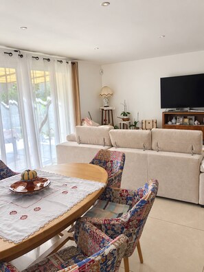 A living room with a sofa, a television, and a dining table with chairs.