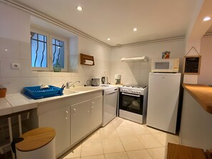 A compact kitchen with white cabinets, a sink, a stove, and a microwave. - Cottage 'Gite La Douceur De Vivre' with Private Terrace, Private Garden and Wi-Fi (Domérat)