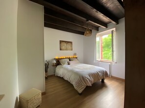 A bedroom with a bed, bedside table, lamp, and a window with a view of greenery. - Cottage 'Gite La Douceur De Vivre' with Private Terrace, Private Garden and Wi-Fi (Domérat)