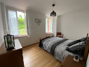 A bedroom with a bed, a chair, a window, and a hanging light fixture.