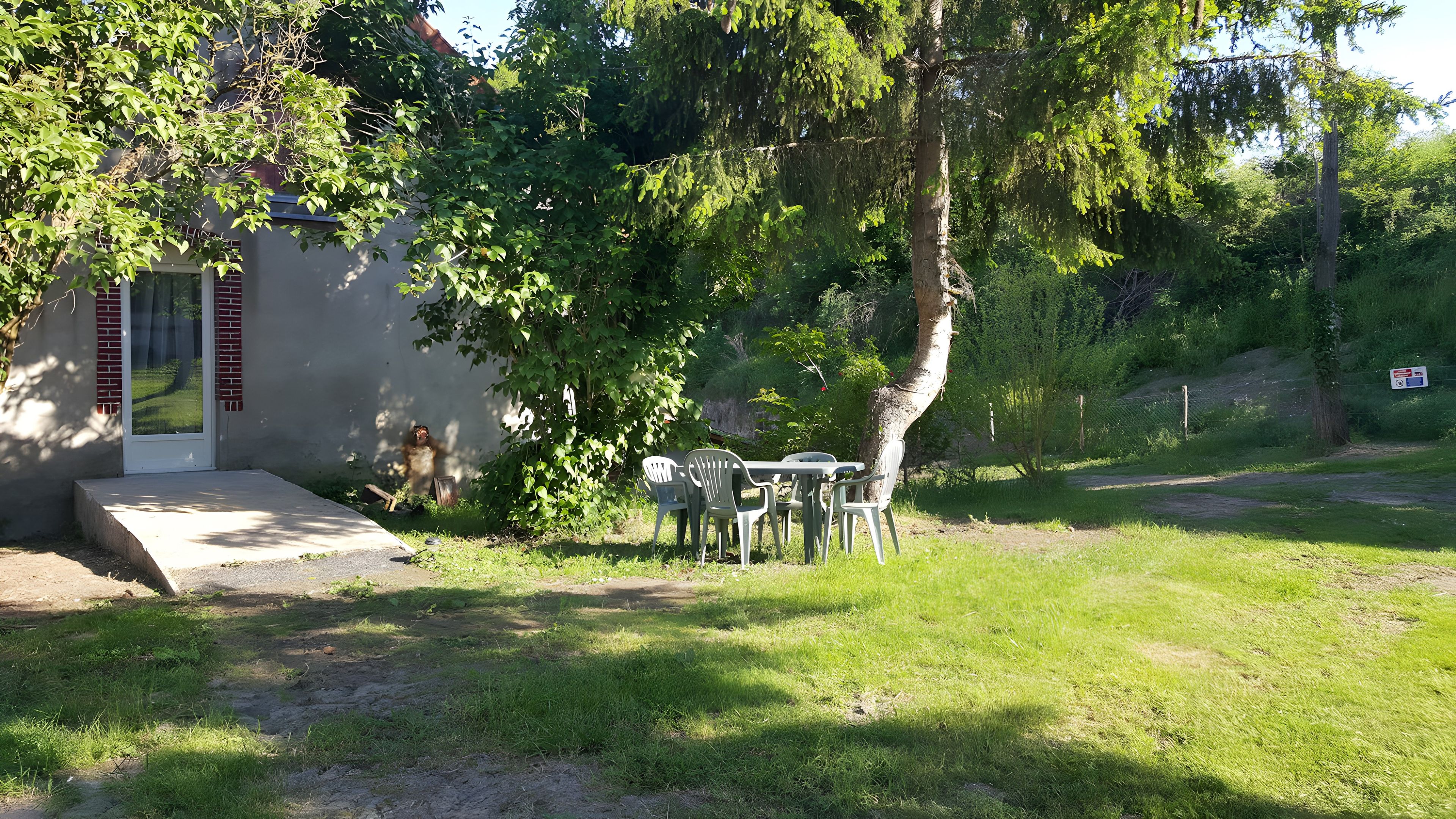 Un petit espace extérieur avec une table et des chaises, un banc en béton et un bâtiment doté d’une porte et d’une fenêtre.