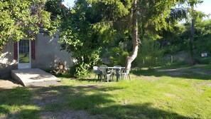 Un pequeño espacio al aire libre con una mesa, sillas, un banco de hormigón y un edificio con una puerta y una ventana.