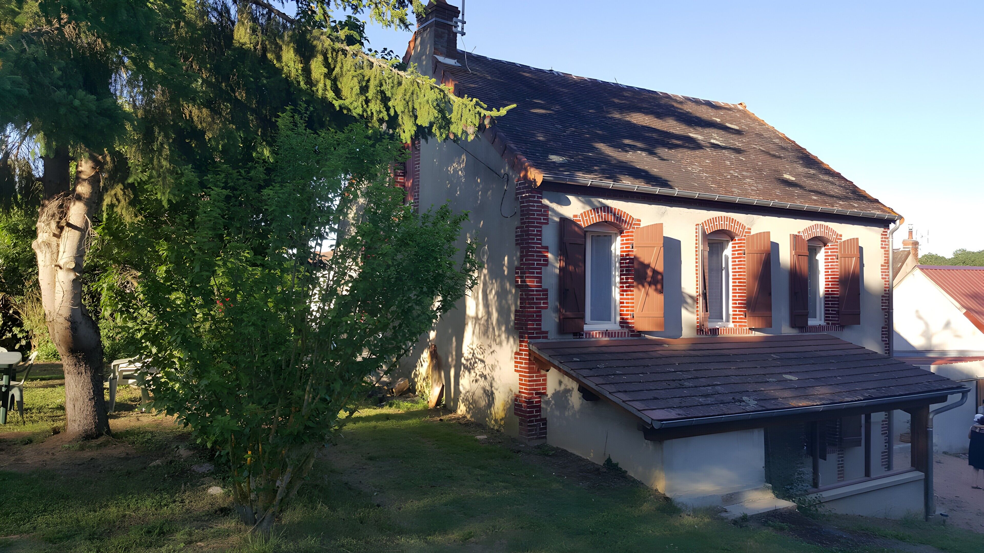 A building with a sloped roof, brick walls, and a small porch with a railing.