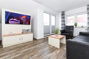 A modern living room with a flat-screen TV, a sofa, a coffee table, and a cabinet. - Holiday apartments "Seagull 4" (Esens-Bensersiel)