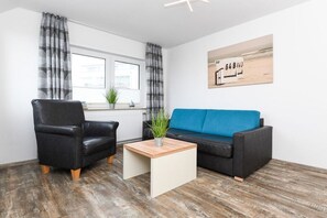 Un salon moderne avec un fauteuil en cuir noir, un canapé bleu et une table basse en bois.
