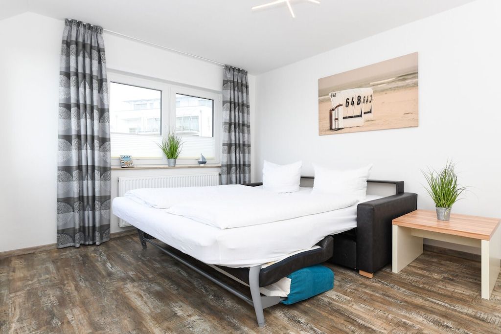 A modern bedroom with a bed, a bedside table, a window with curtains, a radiator, and a wall-mounted artwork.