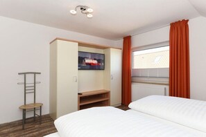 A hotel room with a bed, a wardrobe, a desk, a chair, and a window with curtains. - Holiday apartments "Seagull 4" (Esens-Bensersiel)