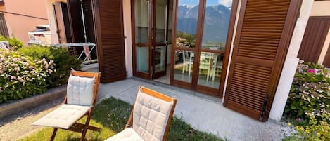 Ein moderner Außenbereich zum Sitzen mit zwei gepolsterten Stühlen, einem Holzboden und Blick auf Berge durch große Glasfenster.