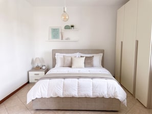 Ein Schlafzimmer mit einem Bett, einem Nachttisch, einer Lampe, einer Uhr und einem an der Wand befestigten Regal mit Dekorationen.