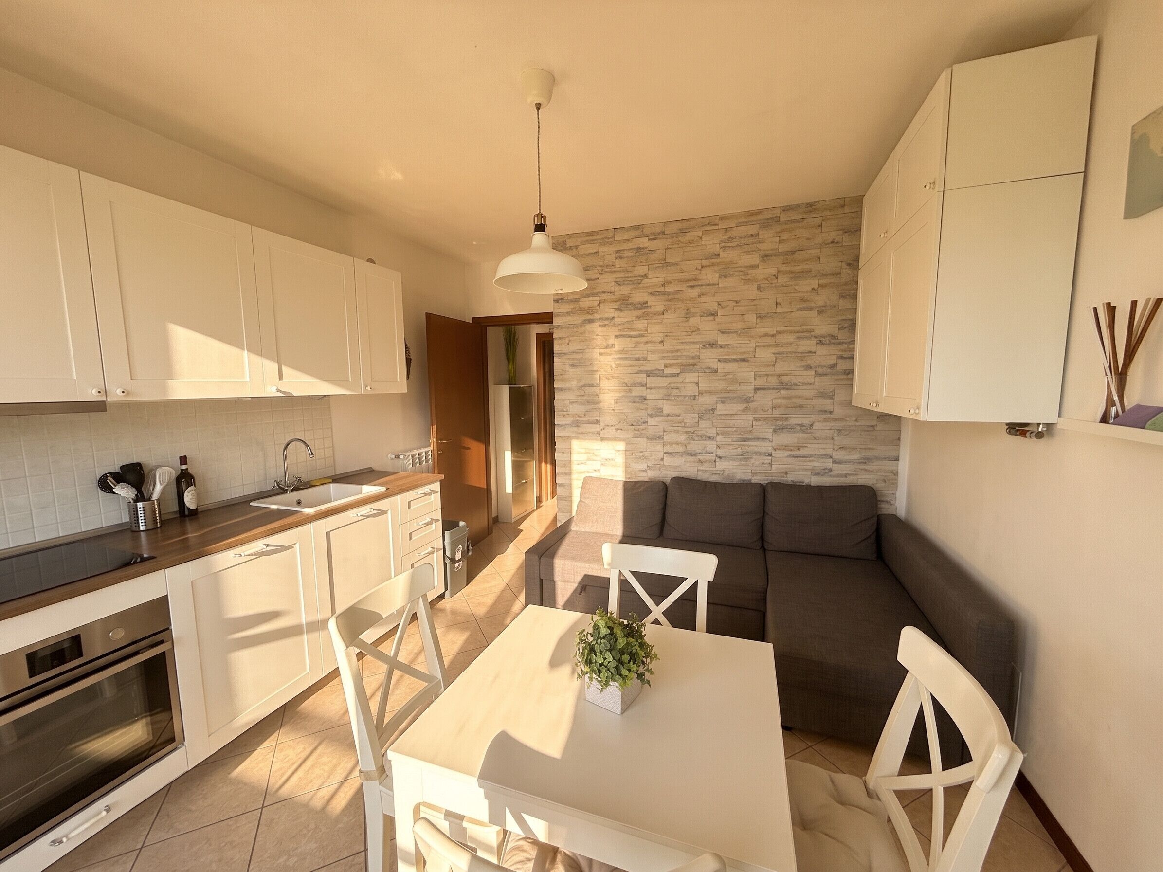A modern kitchen with white cabinets, a dining area with a table and chairs, and a living area with a sofa.
