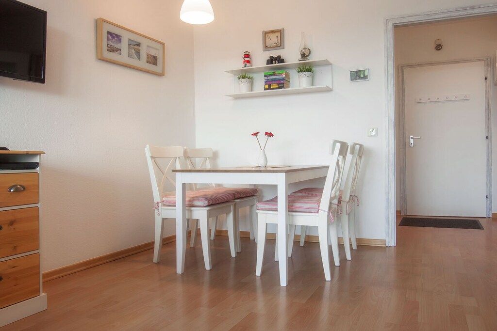 A dining area with a white table and chairs, a television mounted on the wall, and a door to the right.