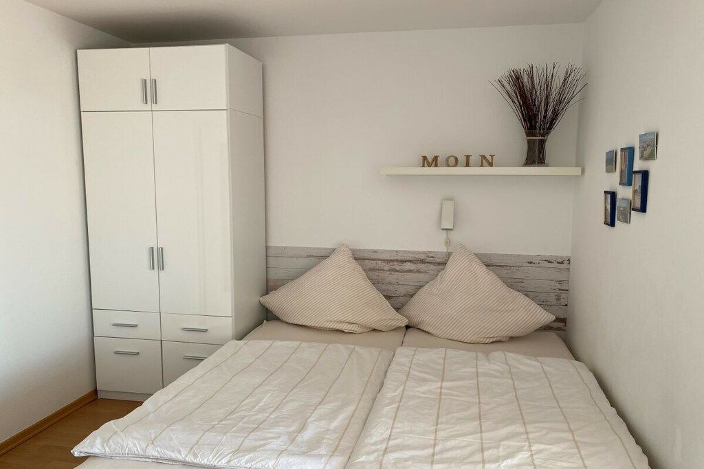 A bedroom with a bed, a wardrobe, a shelf with a nameplate, and a wall-mounted light.