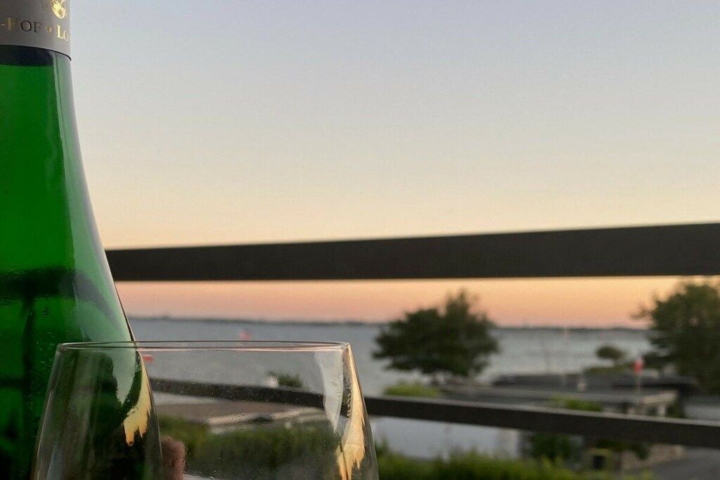 Eine grüne Flasche und ein Glas auf einem Balkon mit Blick auf ein Gewässer und eine Brücke.