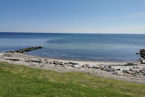 A coastal landscape with a rocky shoreline, clear blue water, and a distant horizon. - “Beach Break” at Haus Hamburg (Großenbrode)