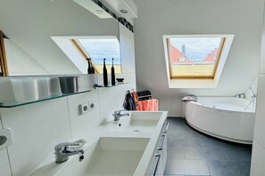 Un bany modern amb un fanal, una banyera independent i un gran lavabo amb mirall.