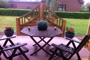 Ein Holz-Sitzbereich im Freien mit Tisch und vier Stühlen, umgeben von Topfpflanzen.