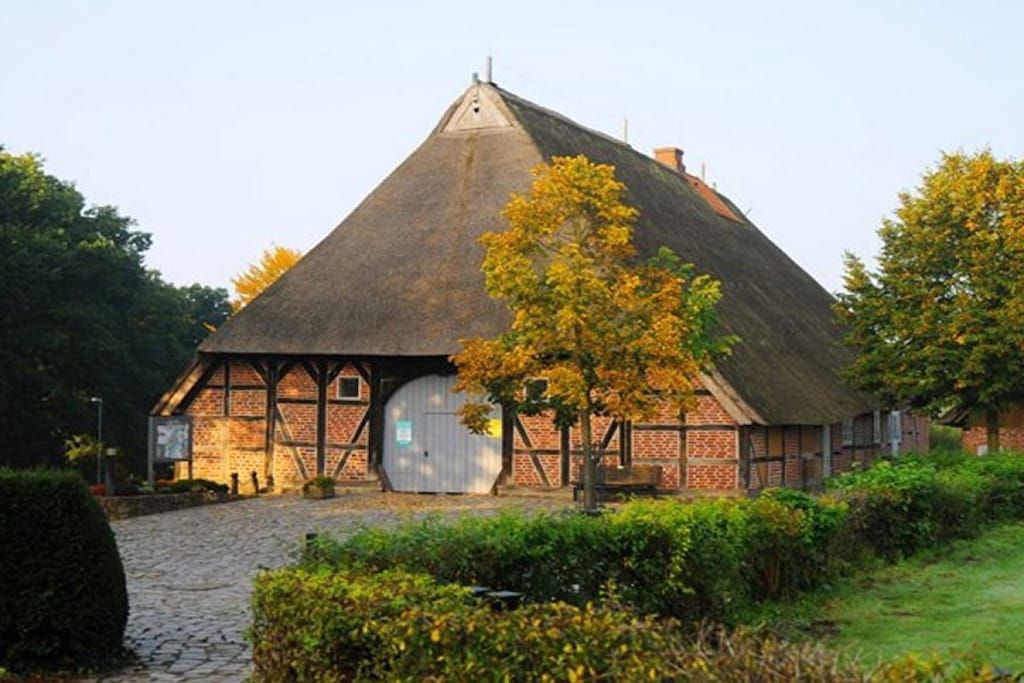 A traditional thatched-roof building with a large wooden door, surrounded by greenery and a cobblestone path.