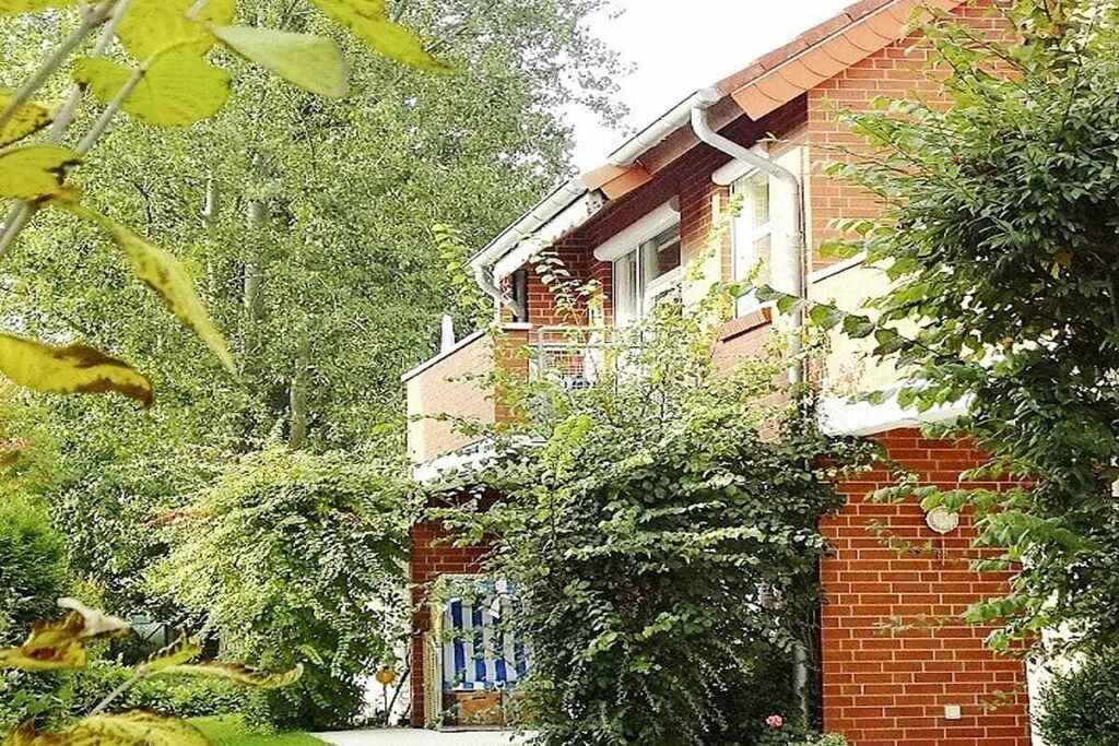 A brick house with a balcony, surrounded by dense foliage.