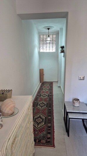 A hallway with a patterned rug, a table with a vase, and a hanging light fixture. - Dar Jasmin: Chic and bright apartment in Marsa (Marsa)